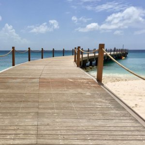 Long wooden jetty curved and with rope railing on Barbados sandy beach and crystal clear water